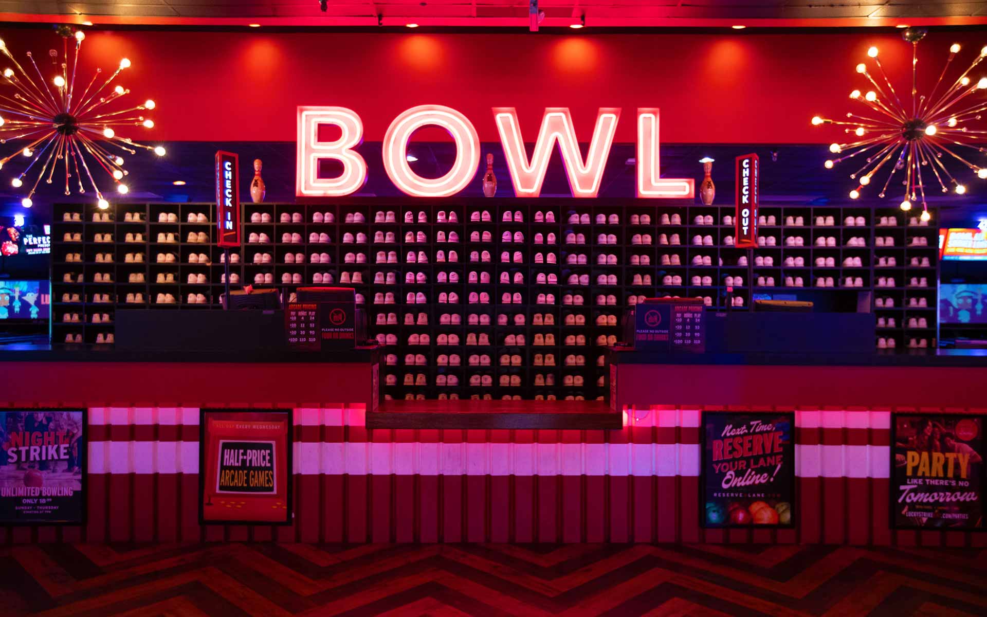 Lucky Strike check-in counter with illuminated “BOWL” sign and wall of bowling shoes in a modern bowling center.