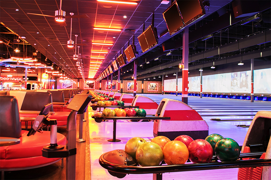 Colorful bowling balls on return rack with bowling center in the background.