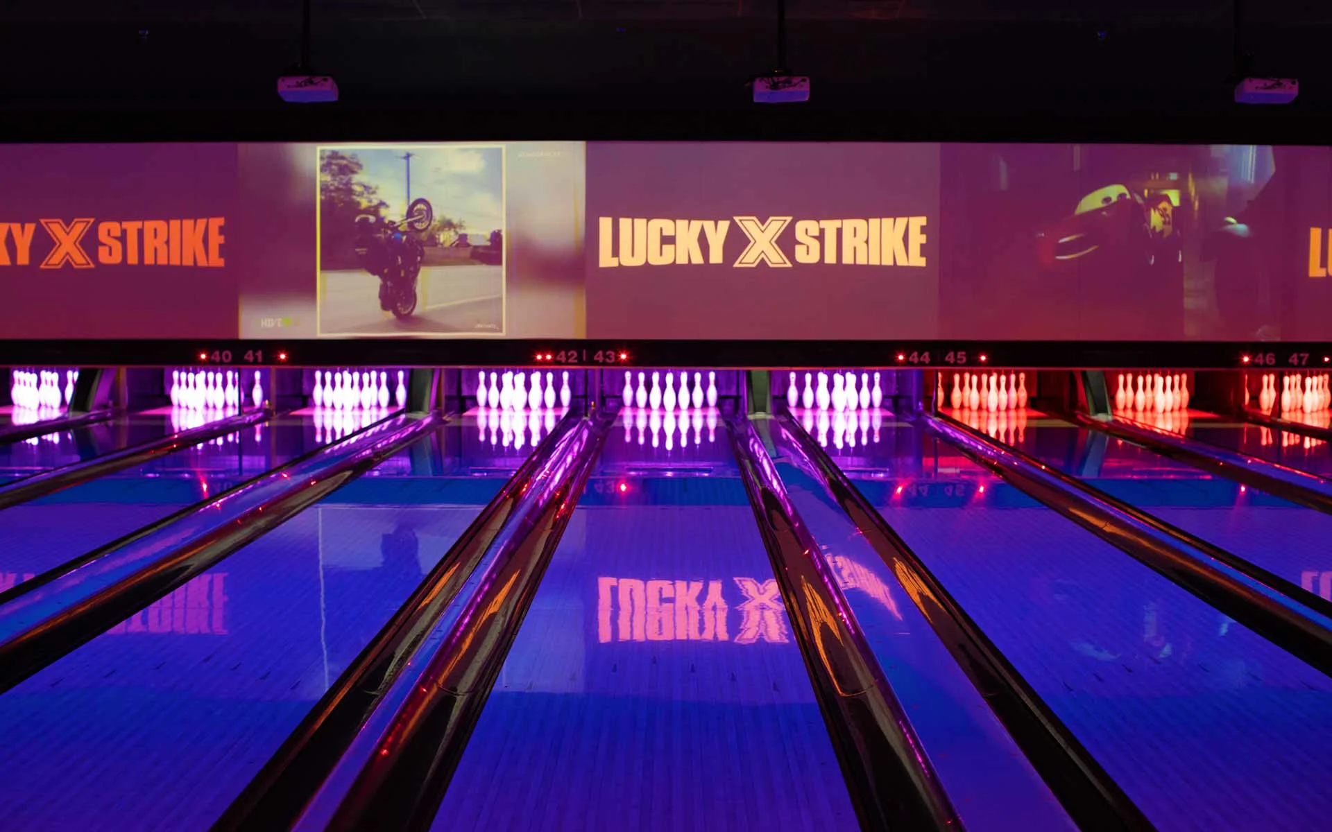 Lucky Strike bowling lanes with glowing pins, large digital screens, and neon lighting in an upscale bowling alley.