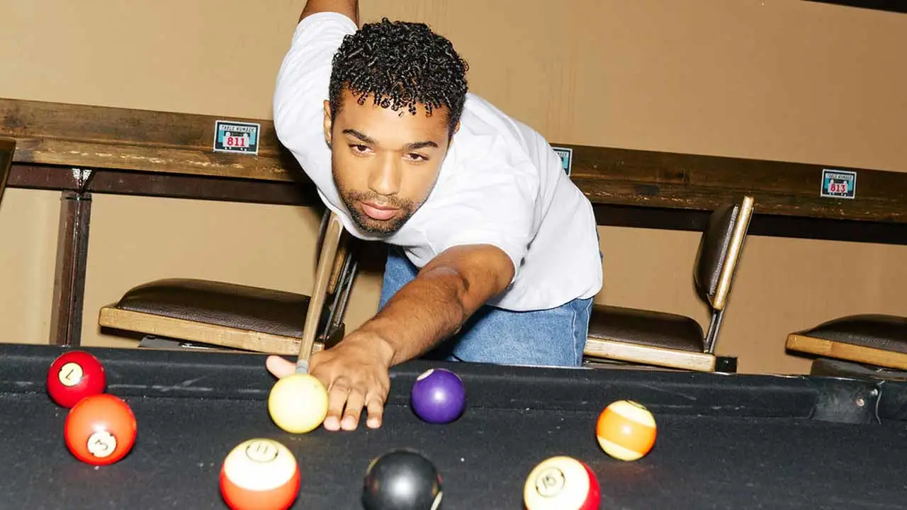Man leaning over pool table lining up a shot at a bowling center.