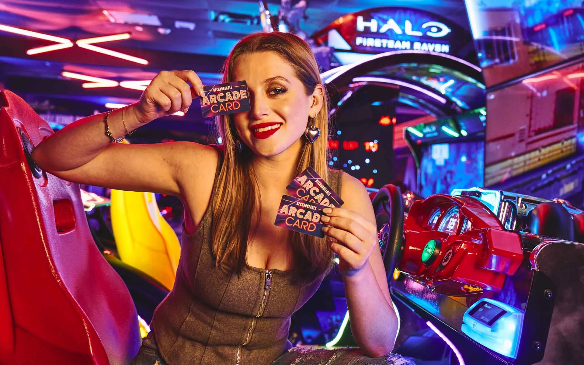Woman holding multiple arcade cards and smiling in a neon-lit arcade, surrounded by colorful gaming machines and a vibrant entertainment setting.