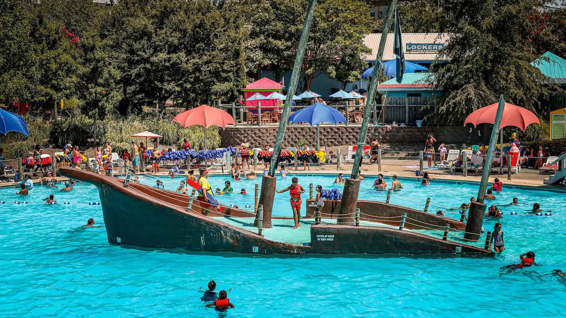 Guests enjoying a wave pool and pirate ship play structure at a busy family waterpark.
