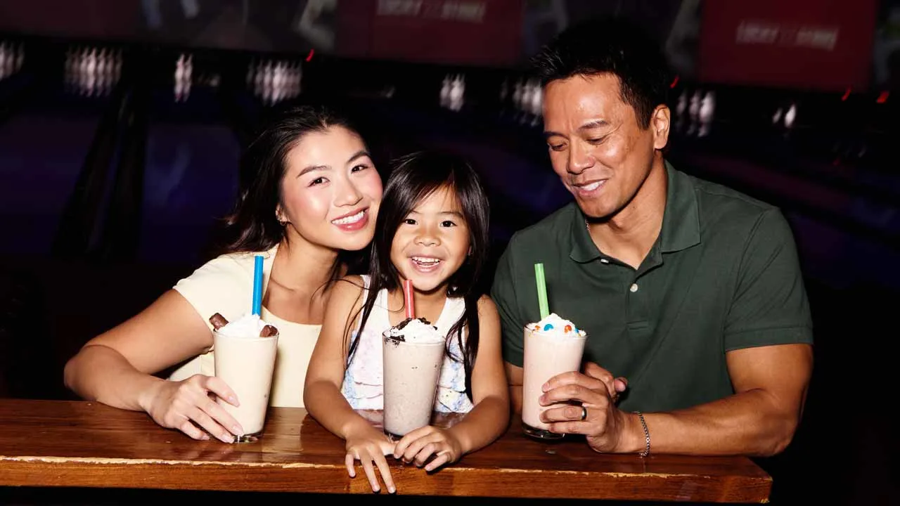 Family of three enjoying milkshakes together at a Lucky Strike bowling center