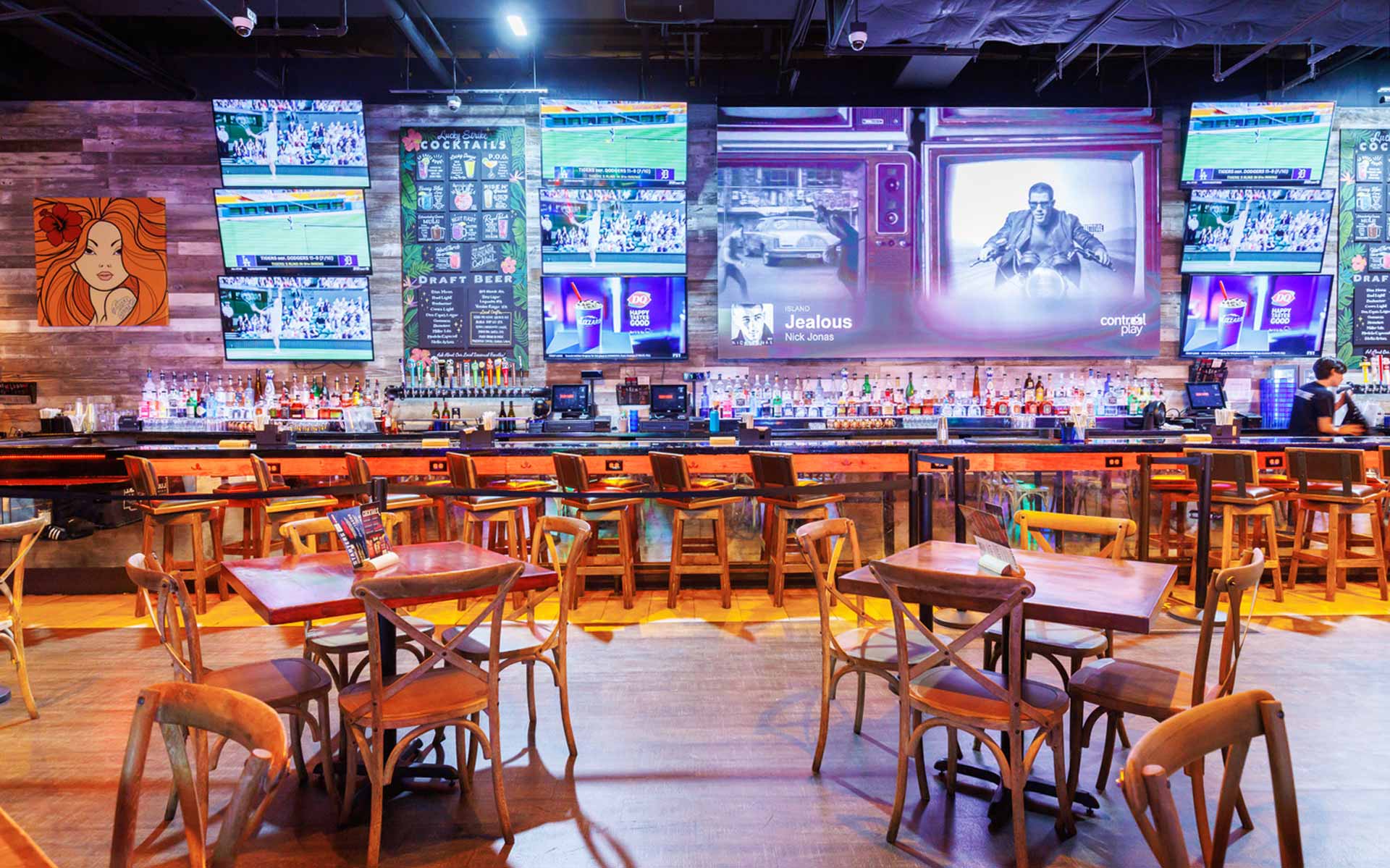 Bright, high-energy bar with extensive seating, wood finishes, and a full wall of TVs. Blends sports bar energy with a polished dining setup—ideal for groups, casual meals, and watching games.