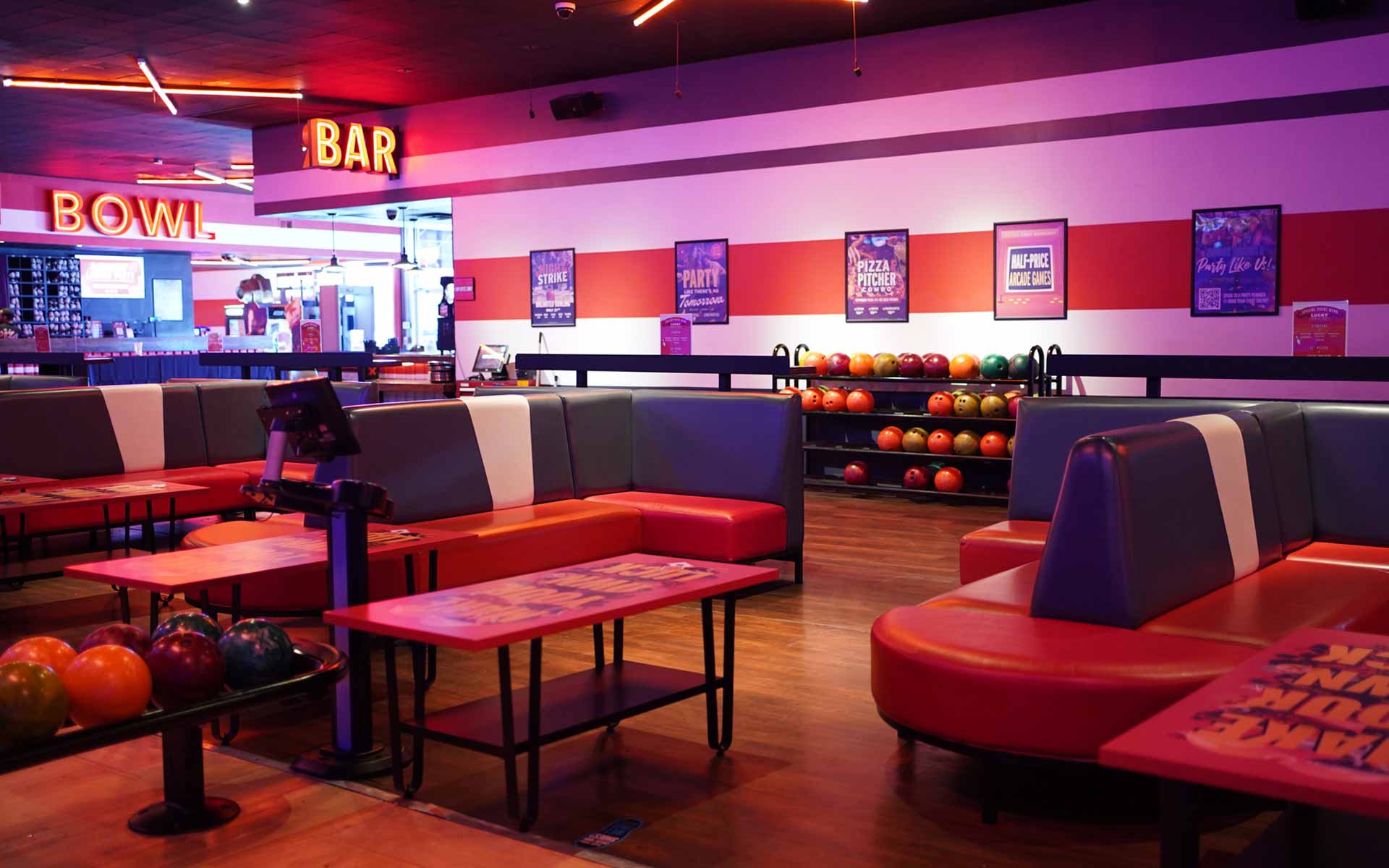 Comfortable lounge seating at Lucky Strike with red booths, tables, and nearby ball racks in a casual social bowling environment.
