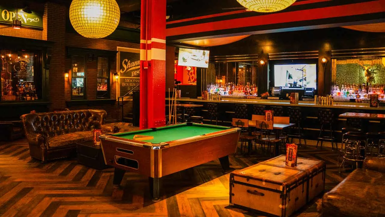 Pool table with lounge seating and a colorful bar in the background at Lucky Strike Times Square.
