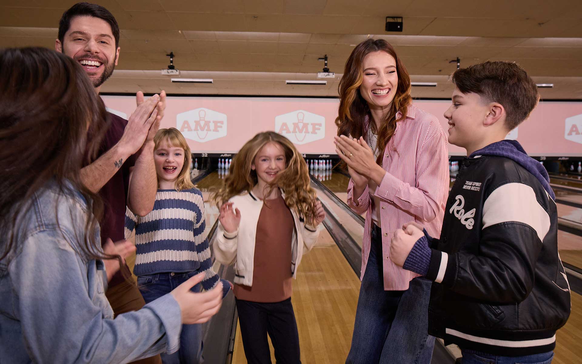 Family of two parents, one boy and three girls cheering after getting a strike at an AMF bowling alley.