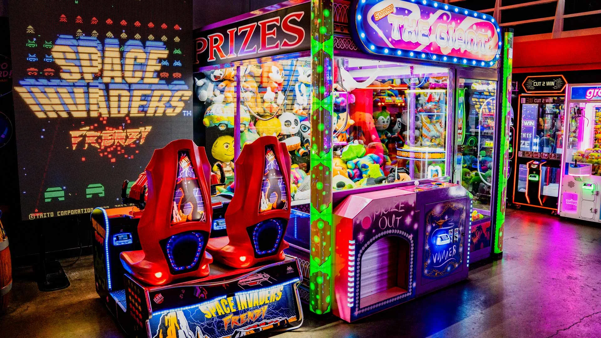Colorful Lucky Strike arcade area featuring Space Invaders Frenzy game, claw machines, and prize redemption games under bright neon lights.