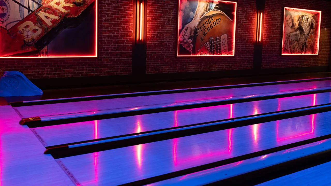 Beautiful bowling lanes with black lights and large neon-lit signs in the background.