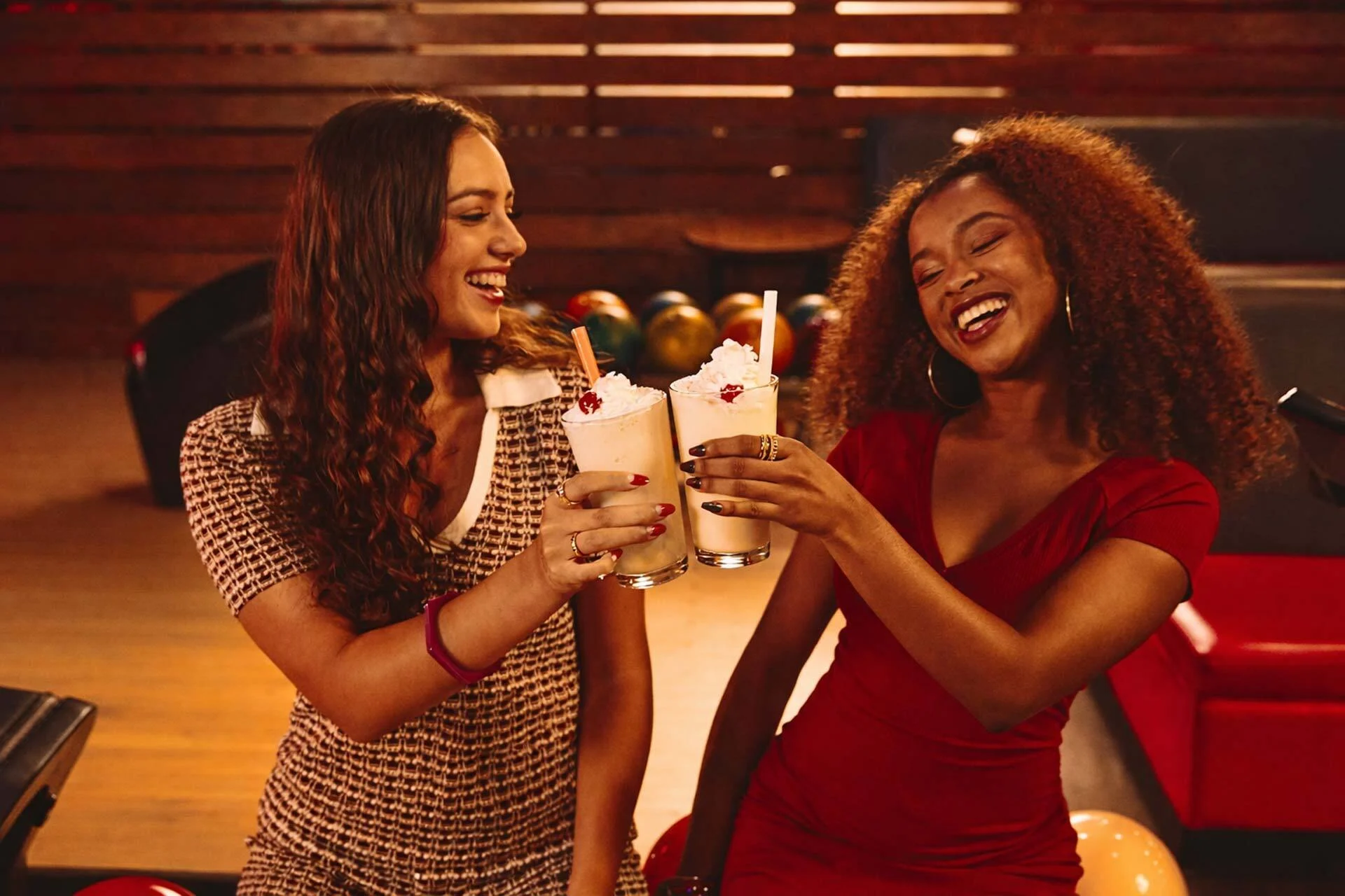 Two girls cheering milkshakes with a bowling alley in the background.