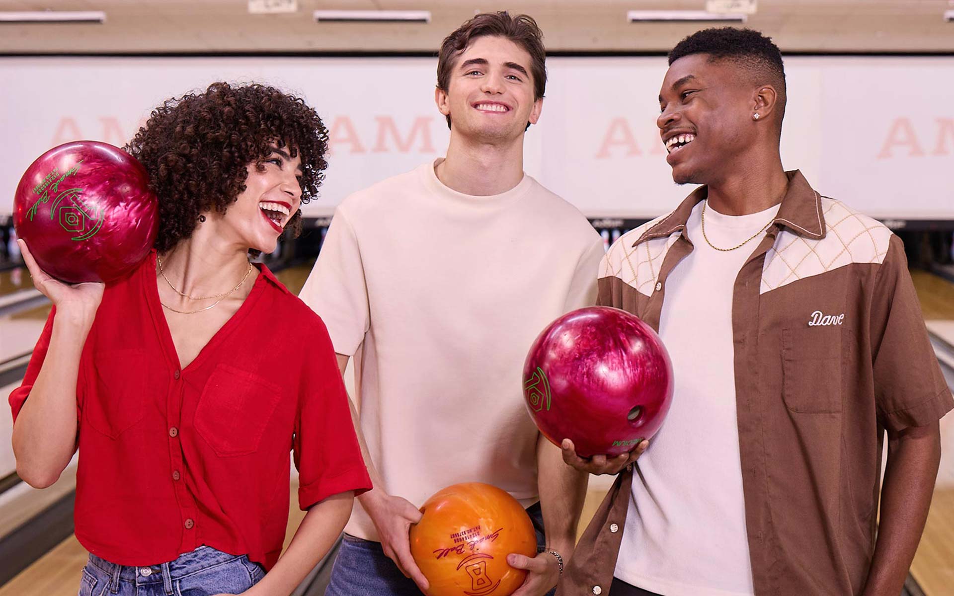 Friends smiling and holding bowling balls while enjoying a fun league night at an AMF bowling center.