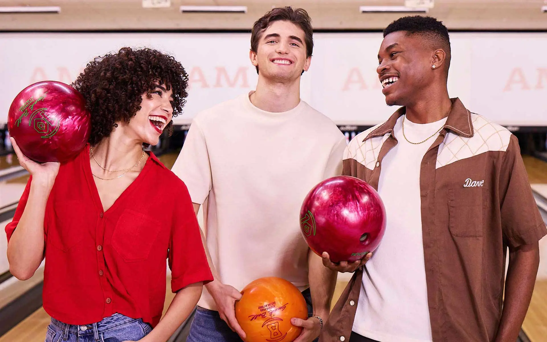 Friends smiling and holding bowling balls while enjoying a fun league night at an AMF bowling center.