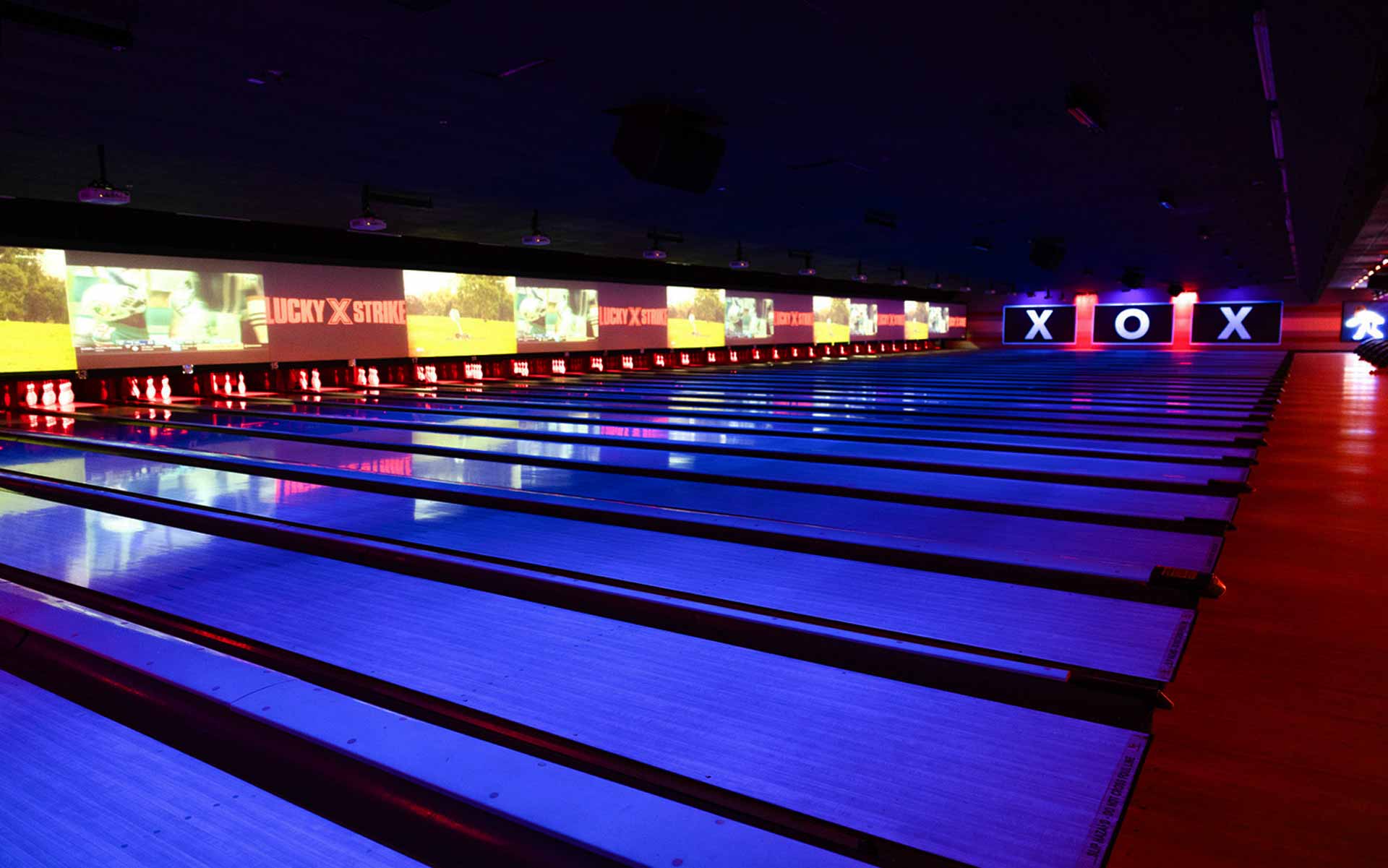 Lucky Strike bowling lanes with neon blue and red lighting, digital scoring screens, and modern entertainment atmosphere,