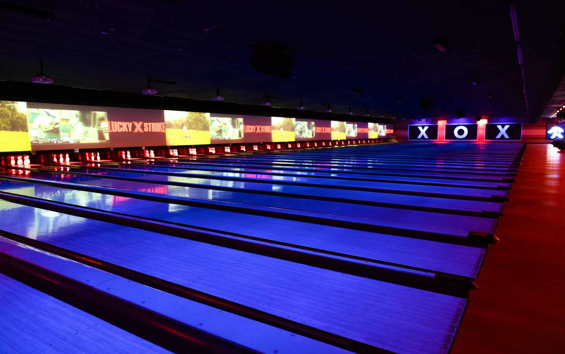 Lucky Strike bowling lanes with neon blue and red lighting, digital scoring screens, and modern entertainment atmosphere,