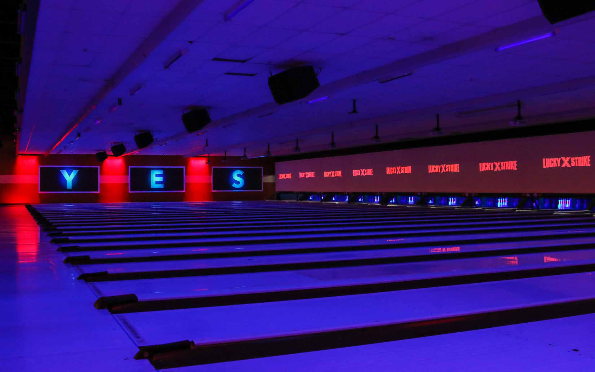 Modern bowling lanes with blue neon lighting, large projection screens, and Lucky Strike branding across the back wall