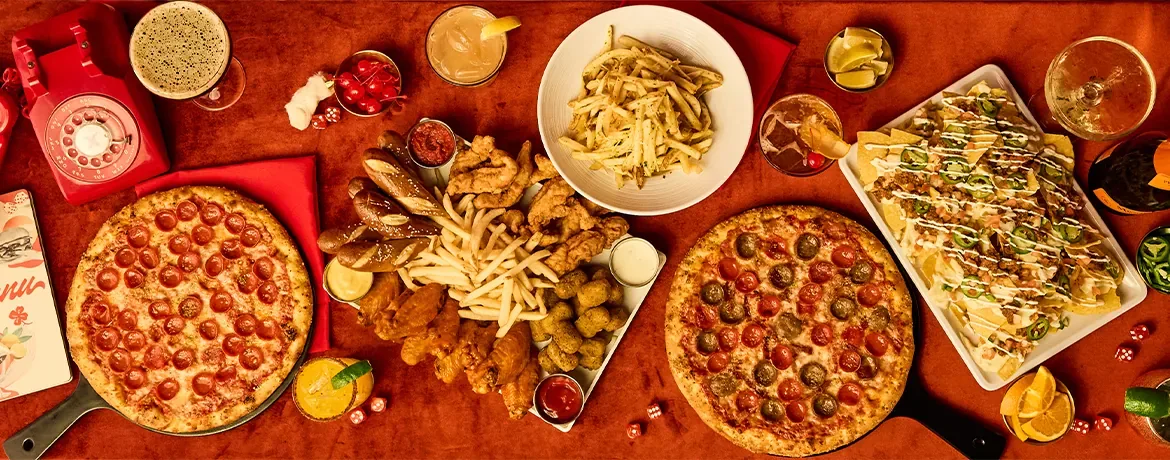Table filled with delicious food: pizzas, nachos, wings, chicken tenders, fries, and drinks