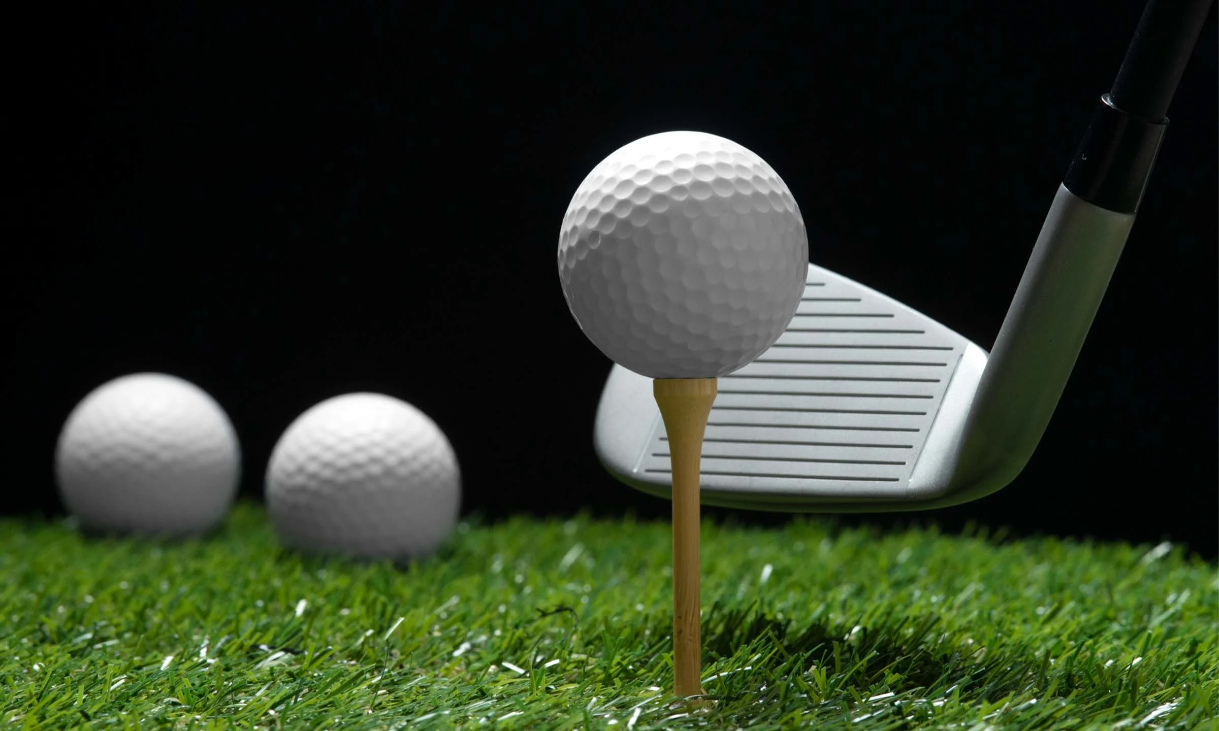 Close-up of a golf ball on a tee with a golf club behind it on artificial grass inside a simulator bay.