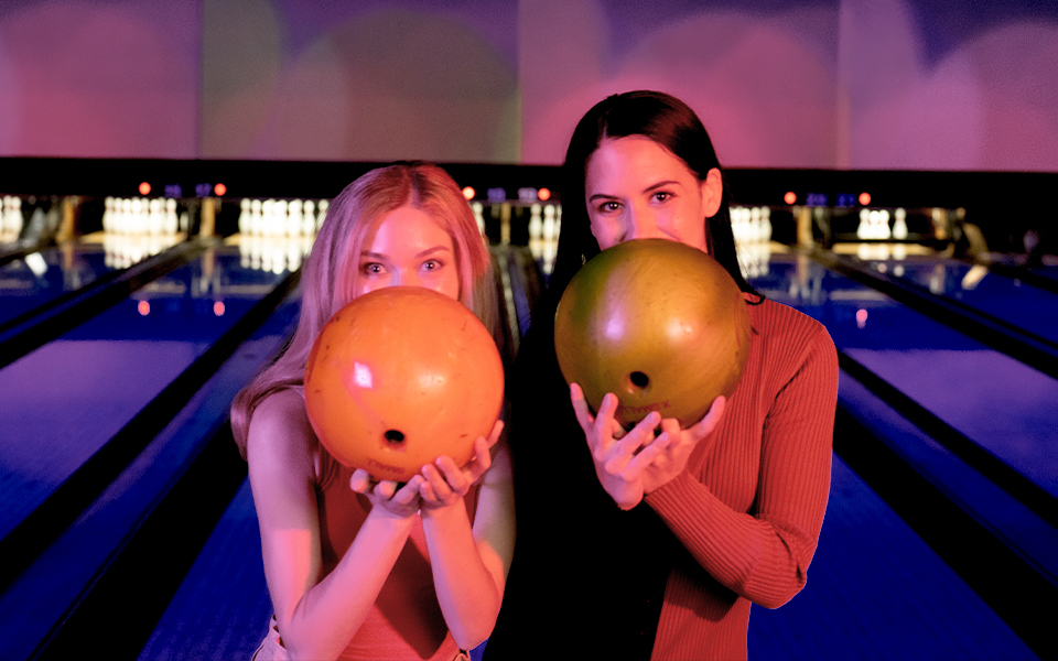 Two women holding bowling balls in front of their faces.