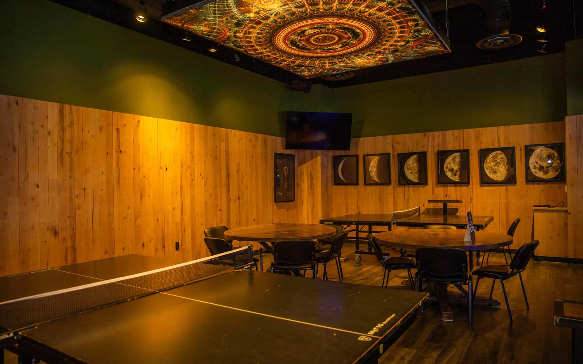 Private lounge area with ping pong table, wooden walls, round seating tables, and ambient lighting at Lucky Strike entertainment venue.