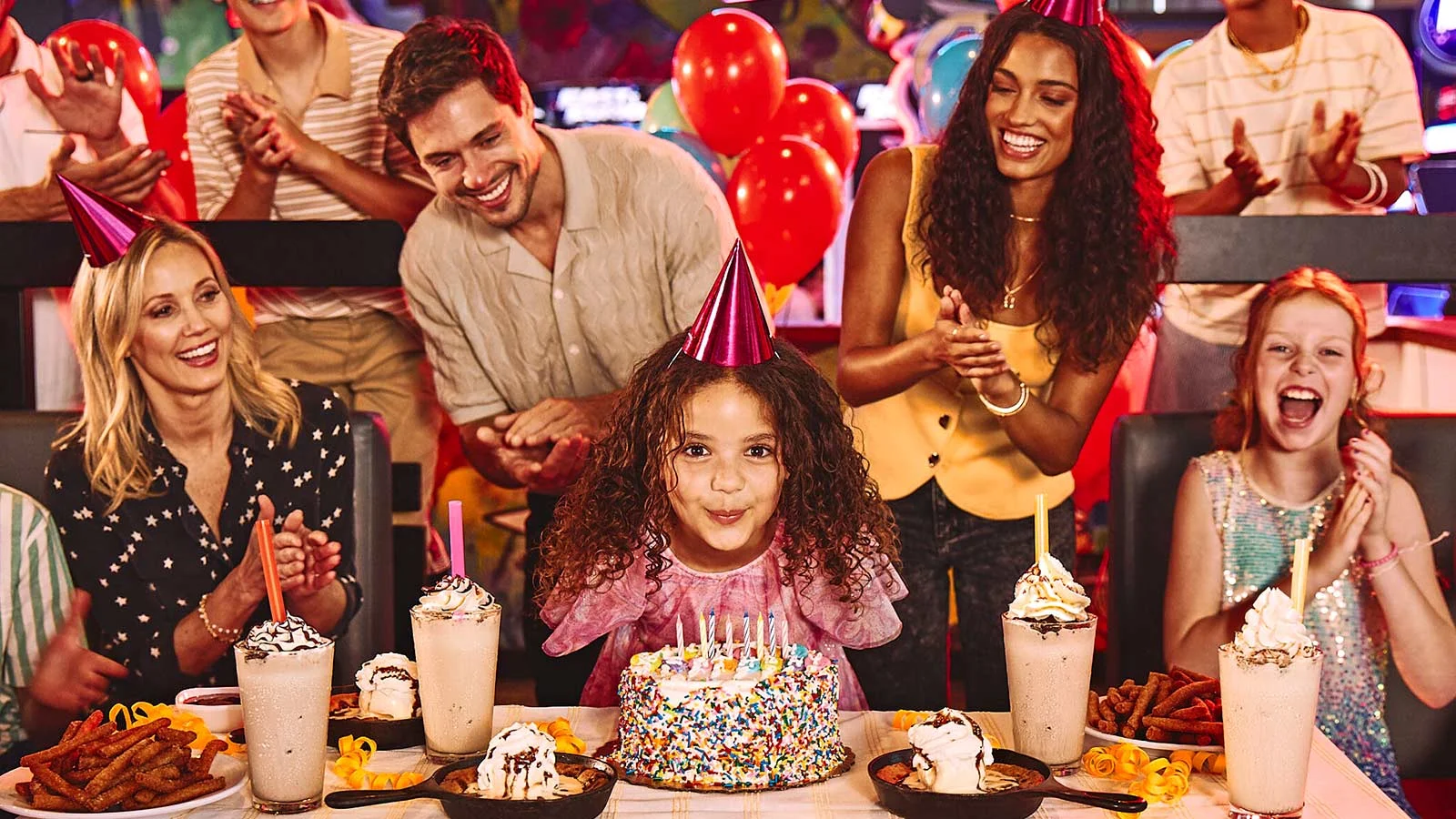 A girl with a birthday cake and a group of people celebrating her birthday party.
