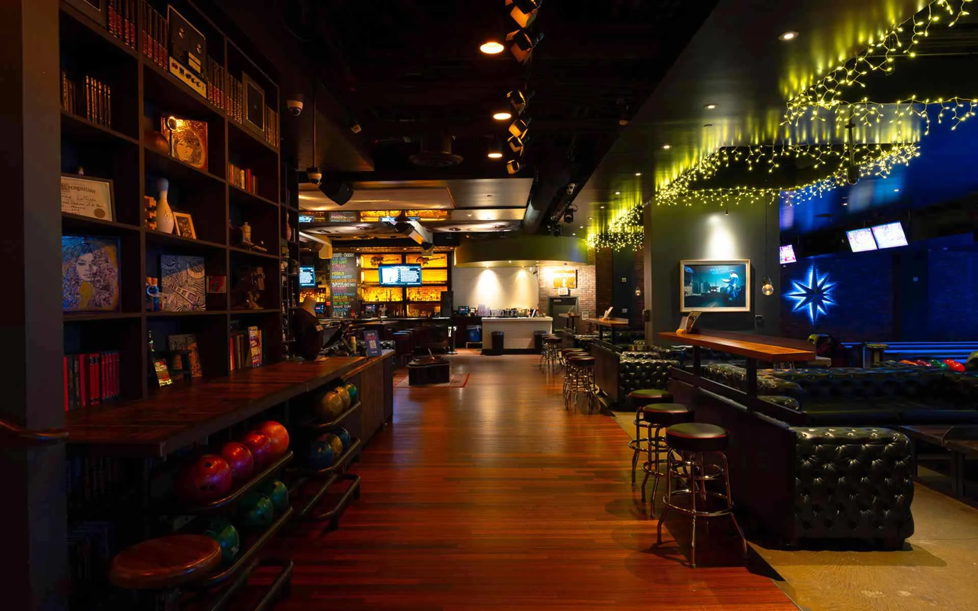 Upscale lounge with rich wood finishes, built-in shelving, and ambient string lighting. Designed for relaxed socializing, this space blends a cocktail bar atmosphere with comfortable seating and easy access to nearby lanes.