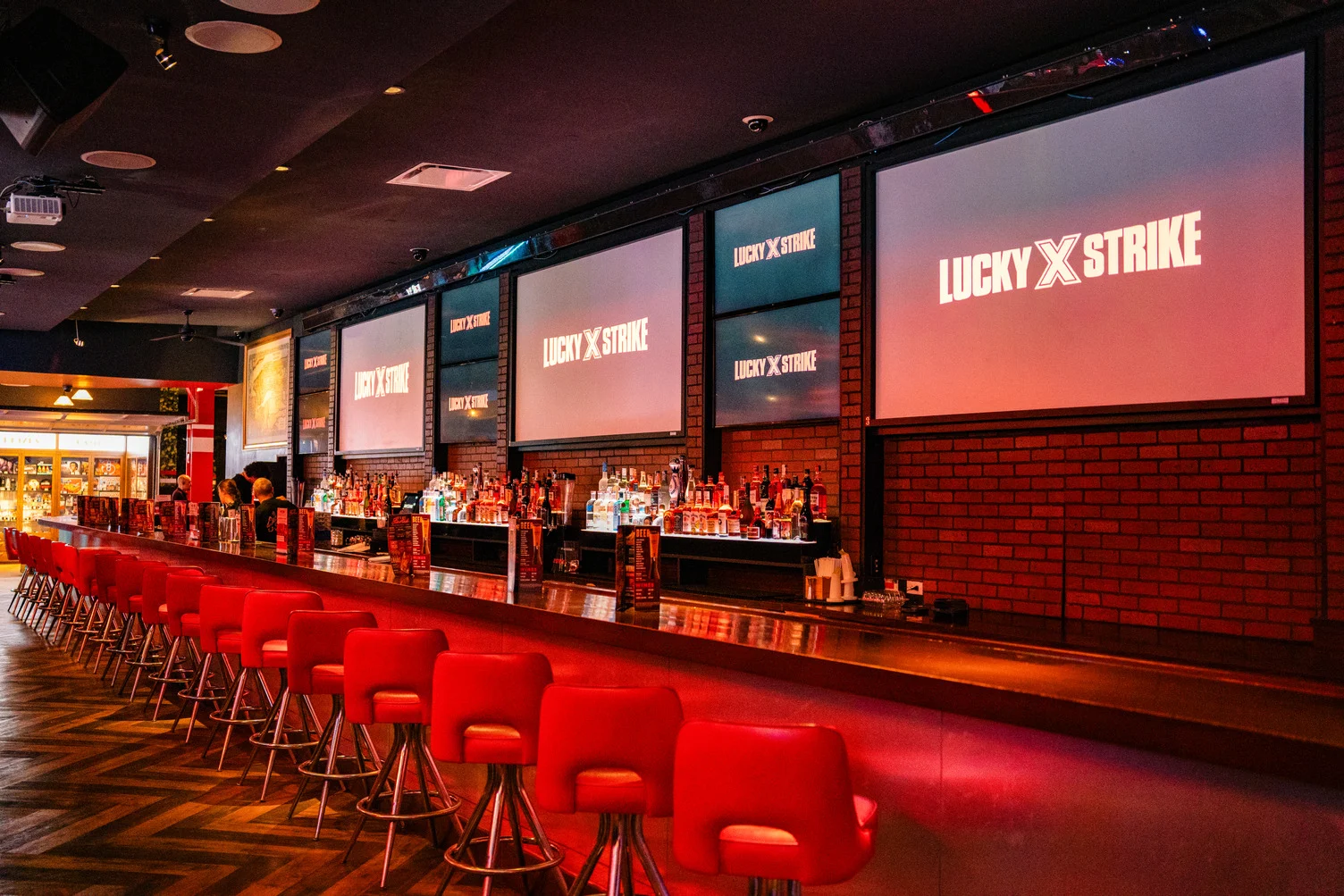 Long bar at Lucky Strike Times Square with red stools, full back bar, and Lucky Strike branded projection screens