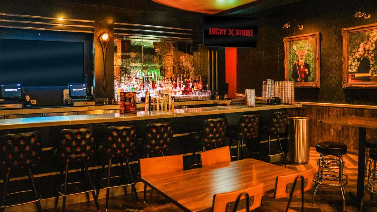 Long bar at Lucky Strike Times Square with red stools, full back bar, and Lucky Strike branded projection screens