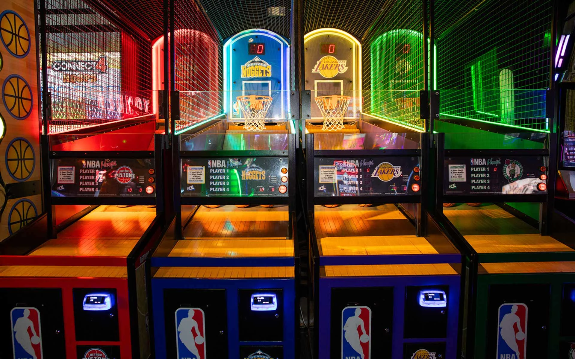Indoor arcade basketball games with NBA-themed hoops in bright red, blue, yellow, and green lanes at Lucky Strike entertainment venue.