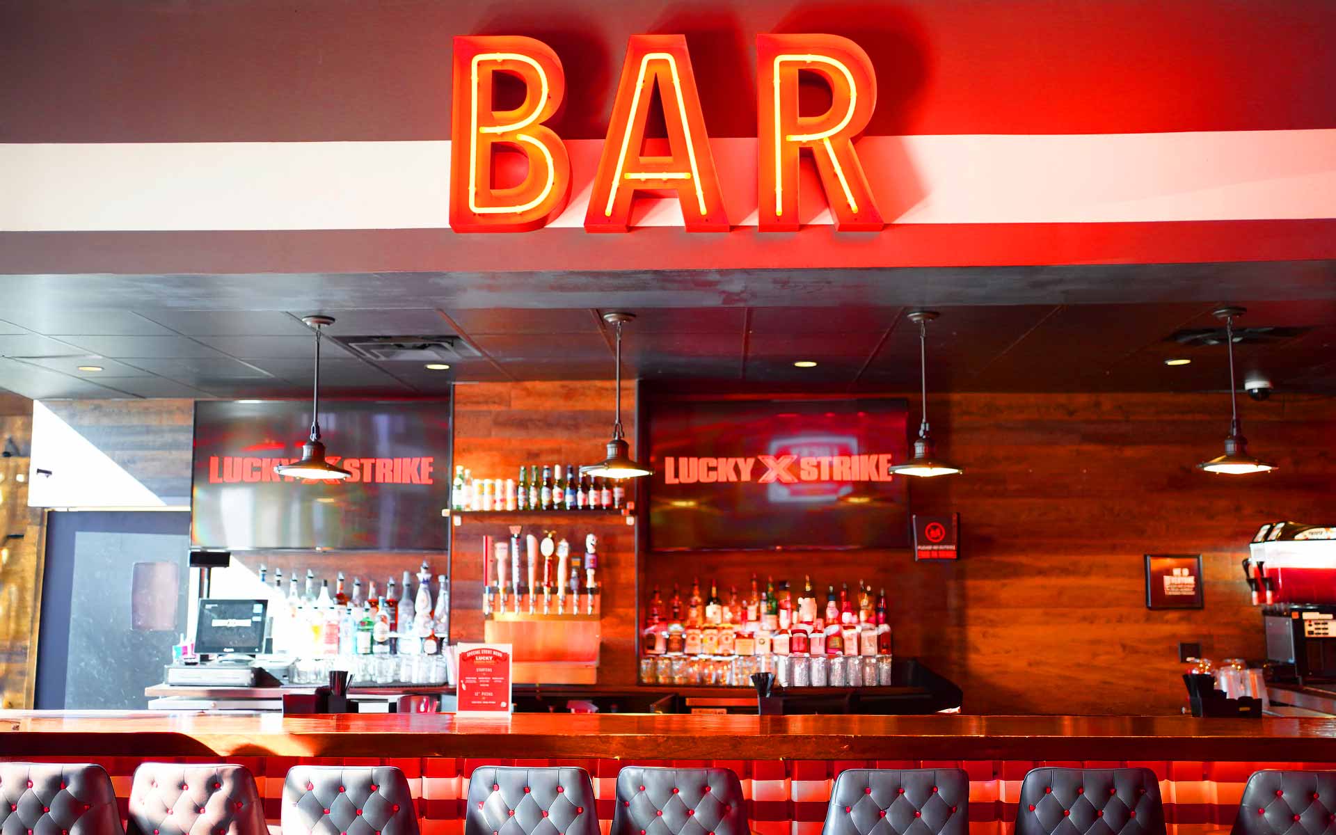 Modern bar at Lucky Strike featuring bold neon “BAR” signage, wood-paneled backdrop, beer taps, liquor display, and stylish seating in a warm, upscale atmosphere.