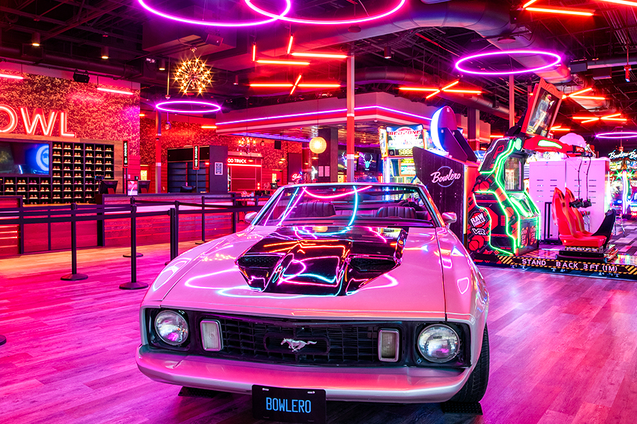 Pink Mustang under neon lights with bowling center in background