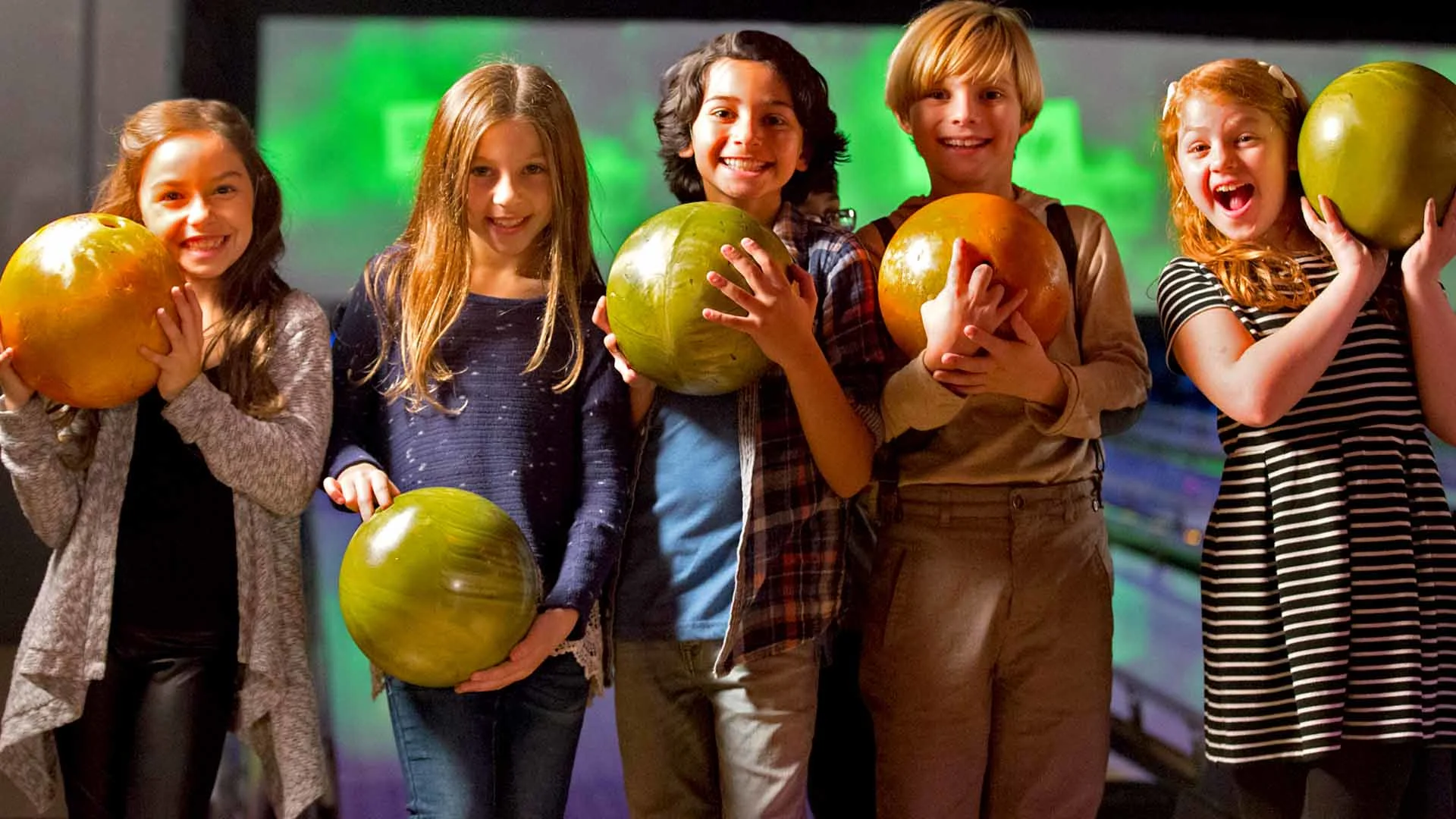 Five kids smiling and holding bowling balls