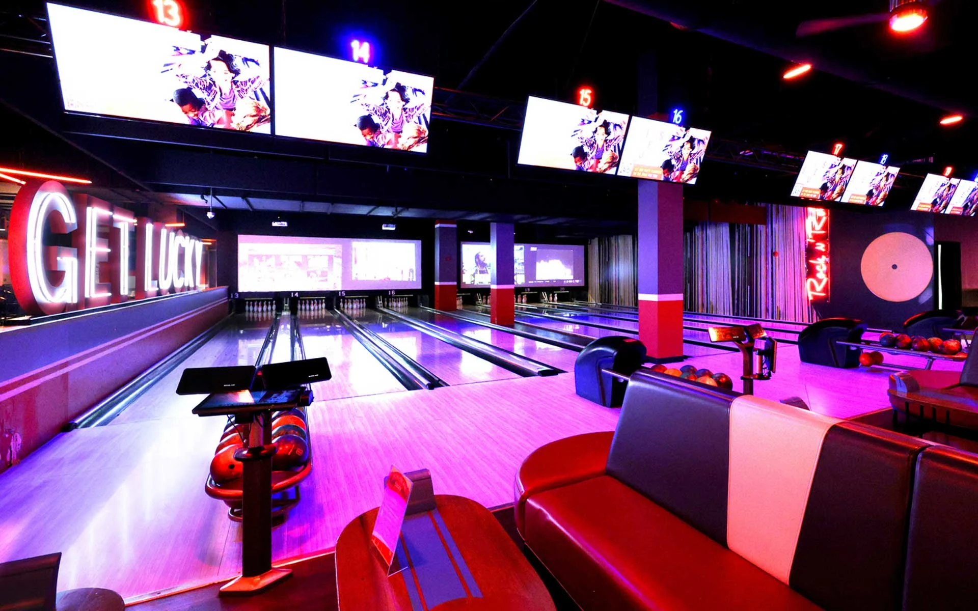 Modern bowling alley with sleek lanes, overhead scoring screens, and neon accents, featuring lounge-style seating and bold “Get Lucky” signage for a high-energy, nightlife-inspired atmosphere.