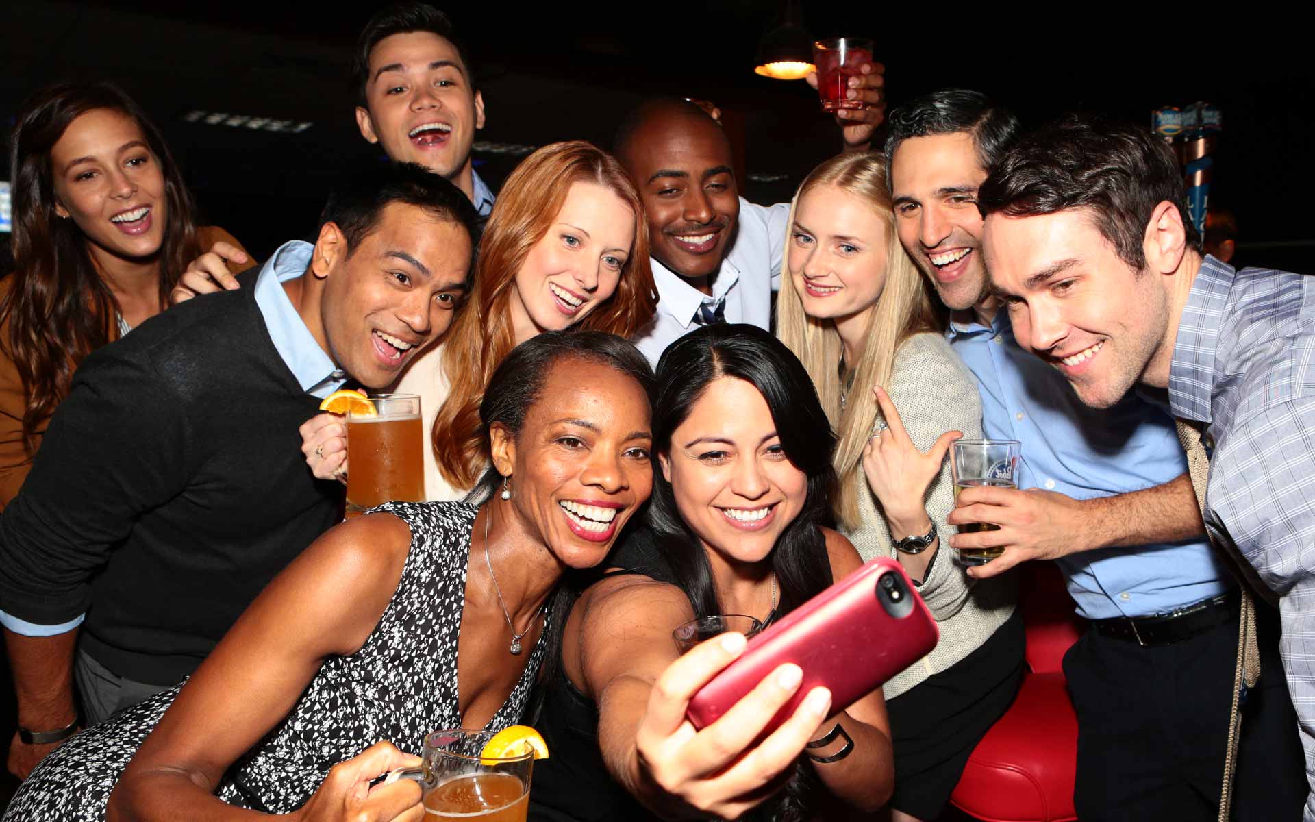 Friends laughing together in a modern bowling lounge with neon lighting, enjoying a social night out on lounge seating.