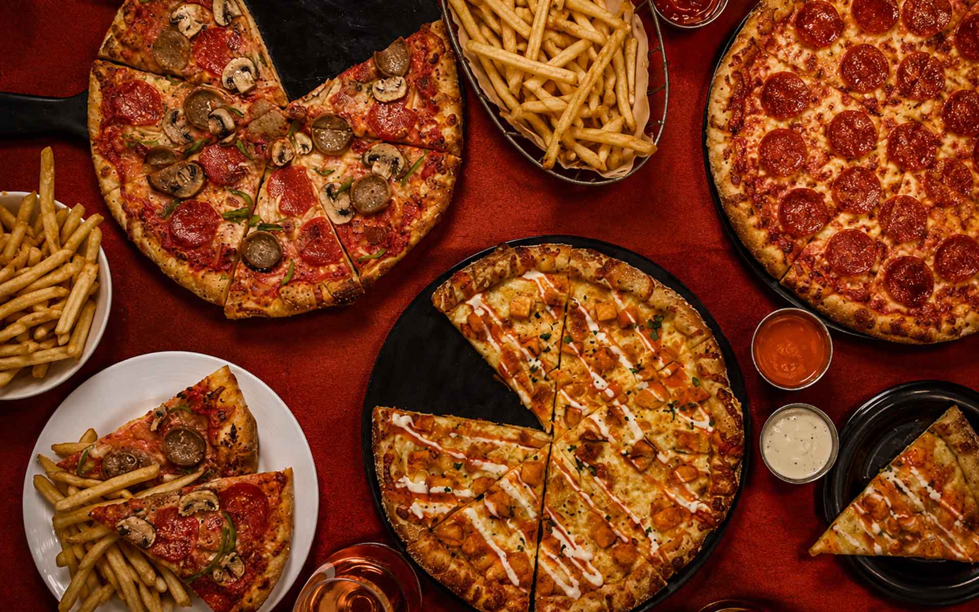 Three pizzas with french fries and dippings sauces.