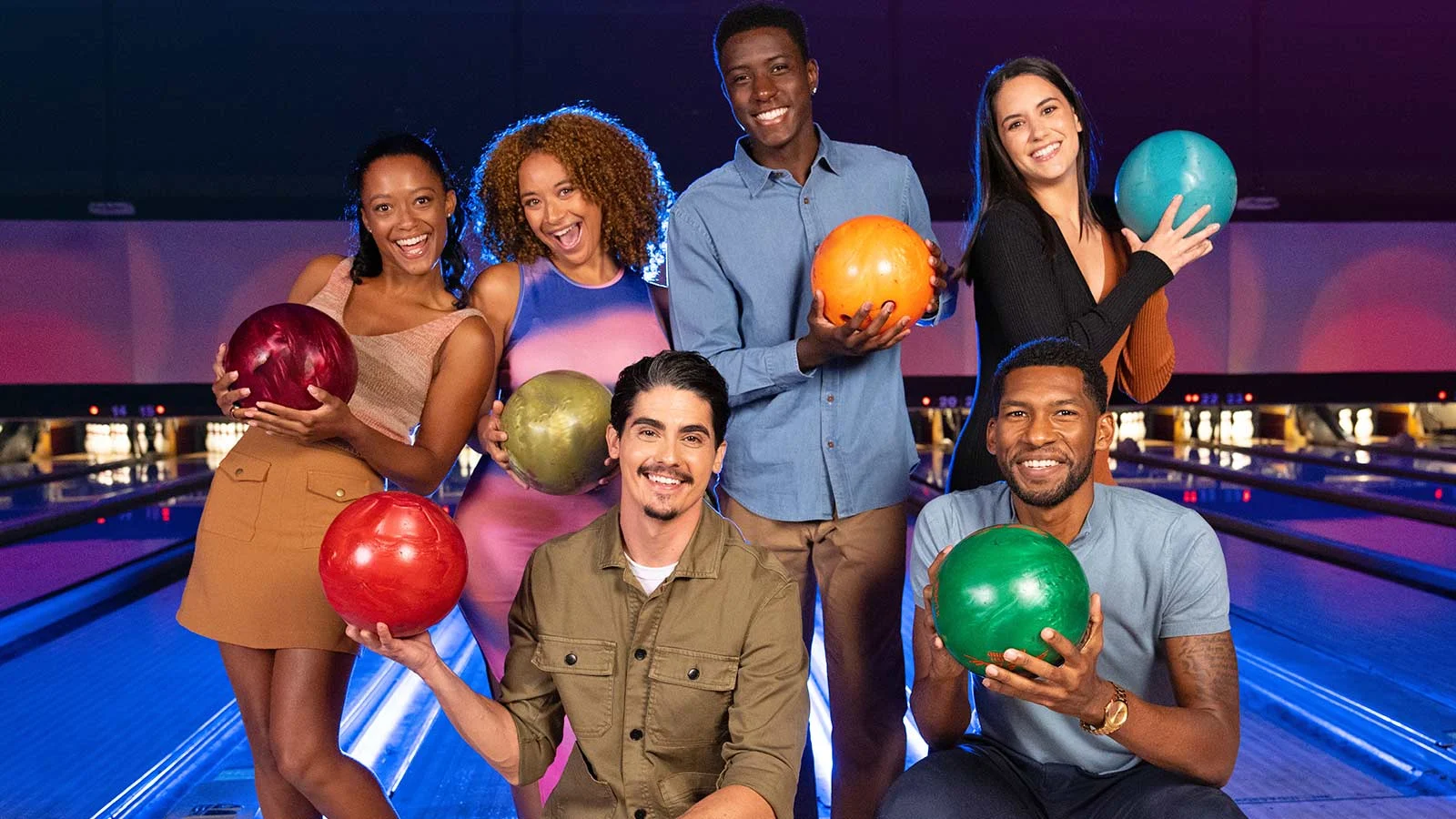 Group of friends holding bowling balls with bowling lanes in the background