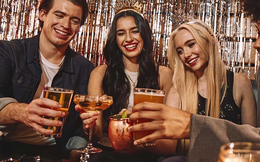 Friends celebrating New Year’s Eve with cocktails, party attire, and festive décor at a lively indoor NYE event.