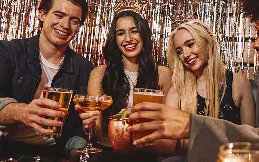 Friends celebrating New Year’s Eve with cocktails, party attire, and festive décor at a lively indoor NYE event.