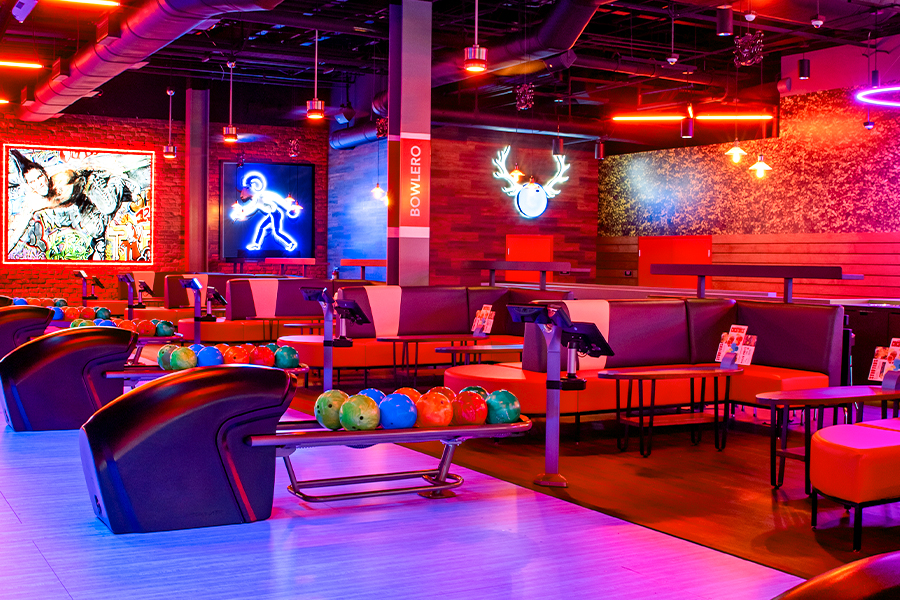 Colorful bowling balls on return rack with bowling center in the background