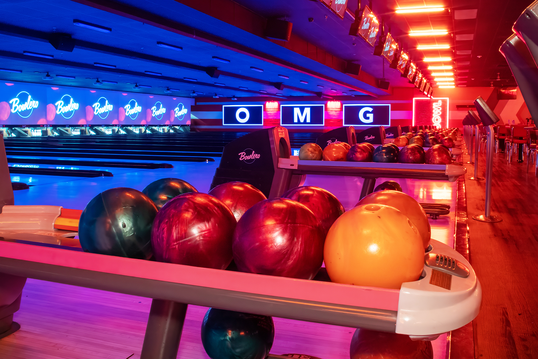 Colorful bowling balls on return rack with bowling center in the background.