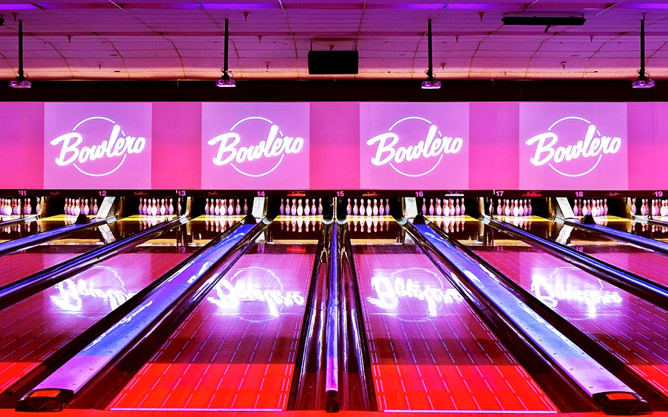 Colorfully lit bowling lanes with Bowlero sings in the background