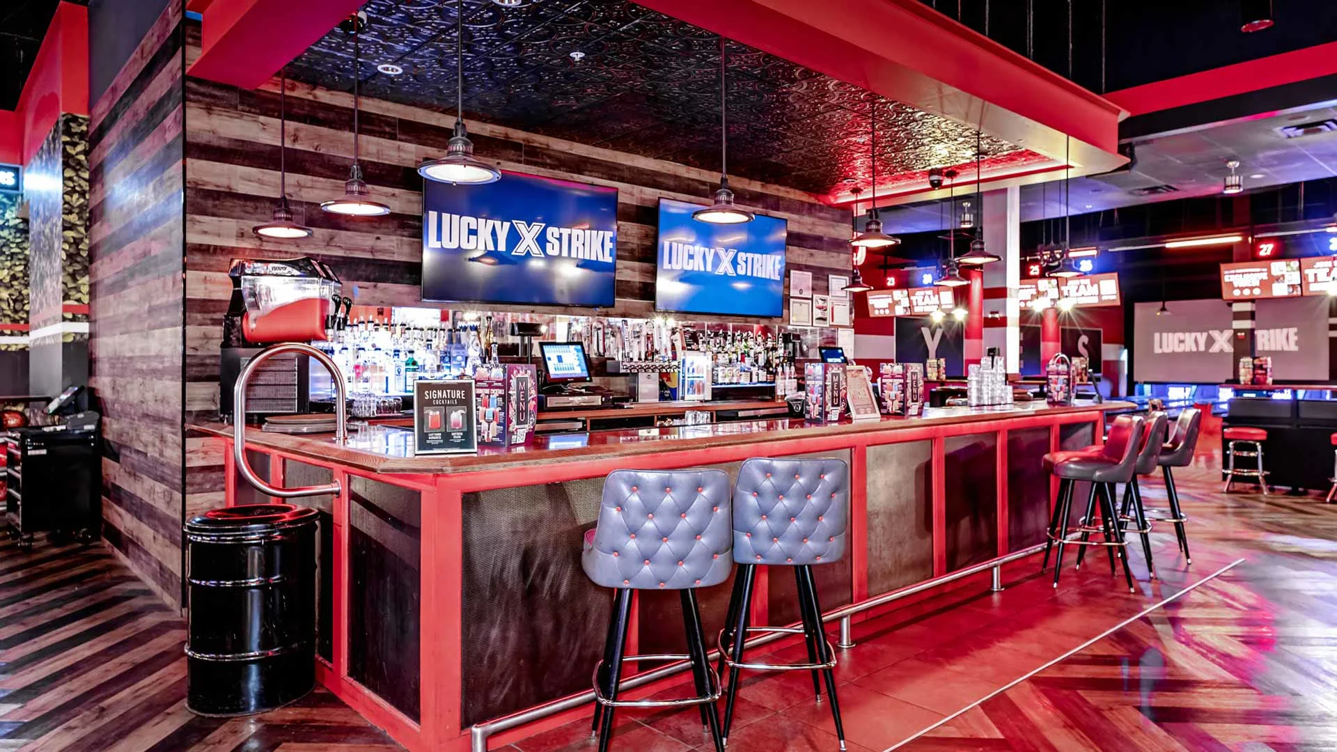 Lucky Strike bar area with a long cocktail counter, bar seating, overhead lighting, and branded digital screens above the back bar.