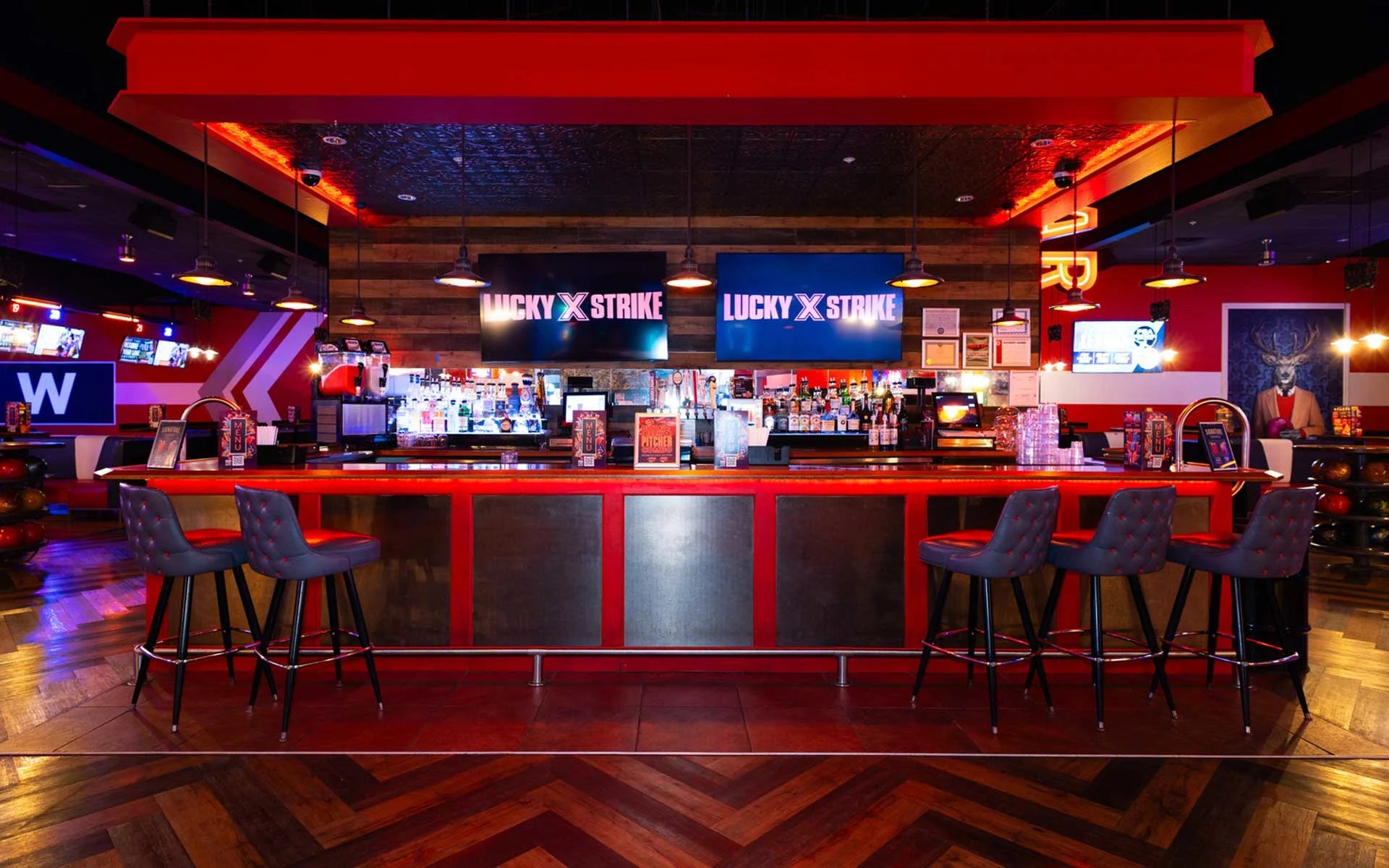 Lucky Strike bar area with a long cocktail counter, bar seating, overhead lighting, and branded digital screens above the back bar.