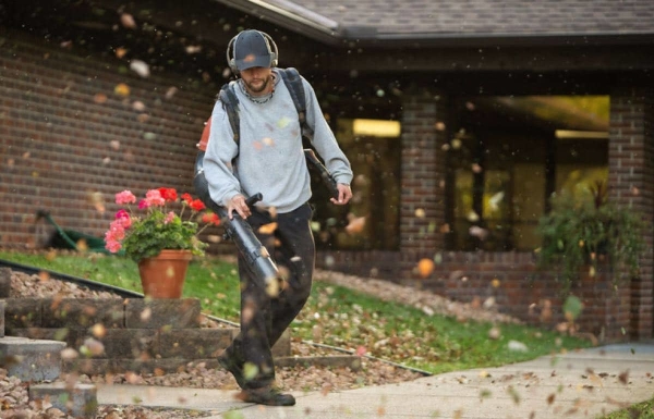 Lawn care pro blowing leaves from a sidewalk.