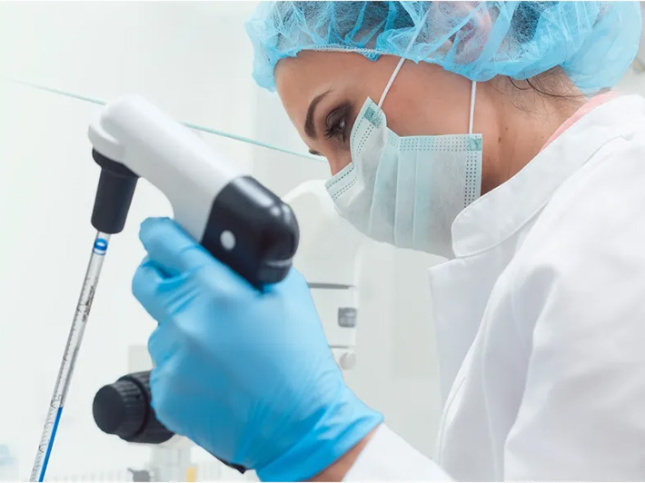 Woman wearing lab protective gear holding a pipette