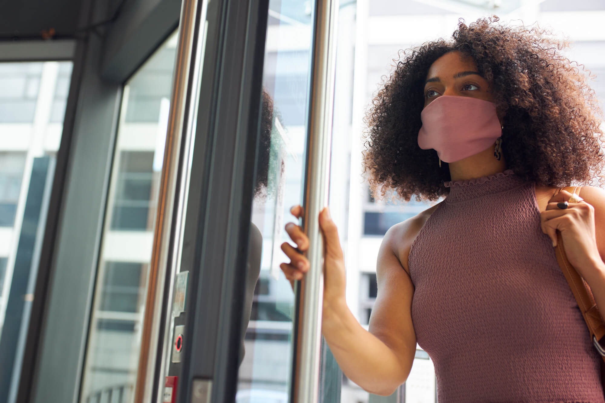 Woman wearing a mask on the street opening a door.