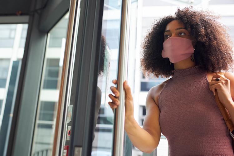 Woman wearing a mask on the street opening a door.