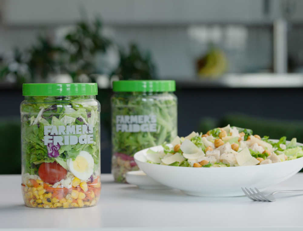 Two jars over Farmer's Fridge salads and a salad in a bowl on a counter. 