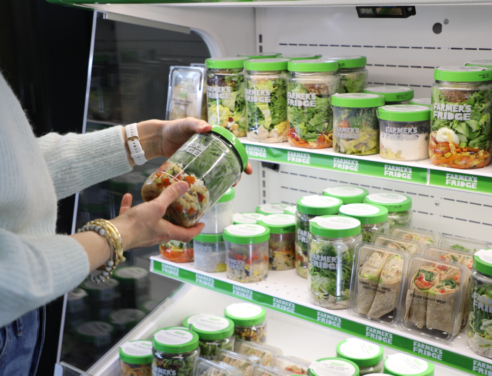 A cooler full of Farmer's Fridge meals with someone picking a salad jar up. 