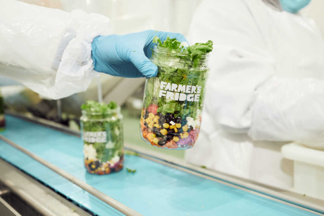 A Farmer's Fridge worker holding a salad in a jar, ready to be shipped off to customers.