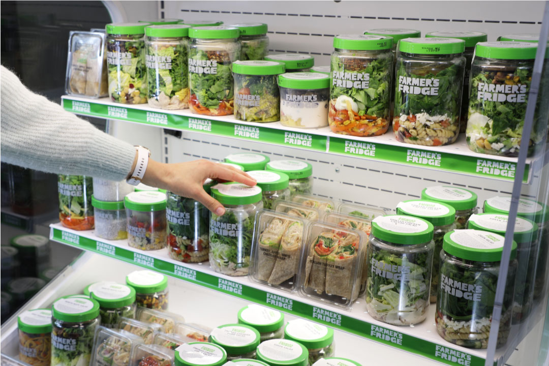 Cooler filled with Farmer's Fridge jars. Someone is standing next to it looking at one of the jars in their hands.